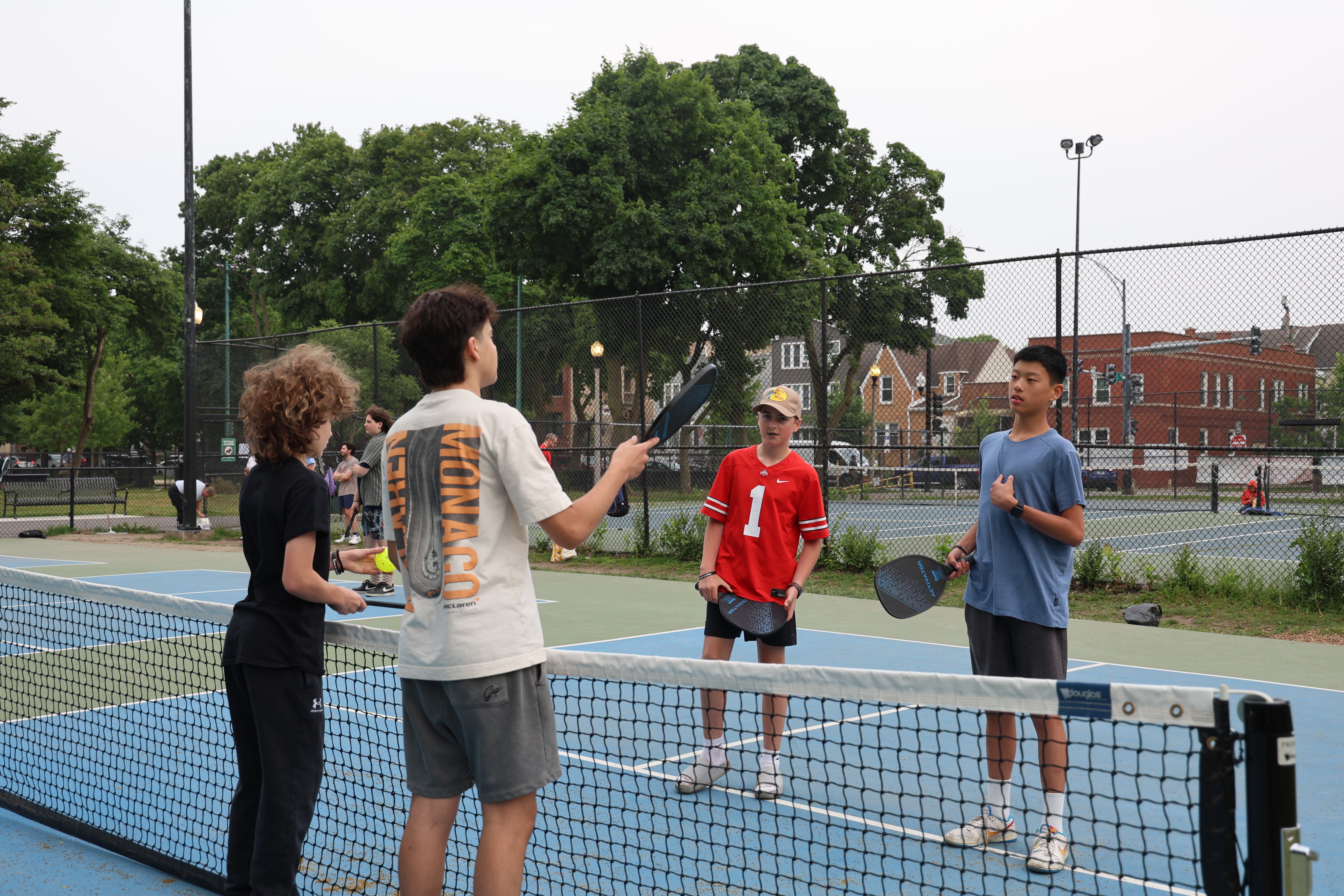 Four boys playing pickleball on a court.